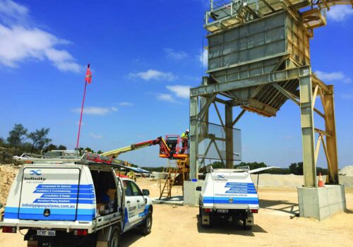 Infinity utes on an industrial worksite outdoors. An Infinity Installation Expert is on an elevated work platform installing blue air pipe.